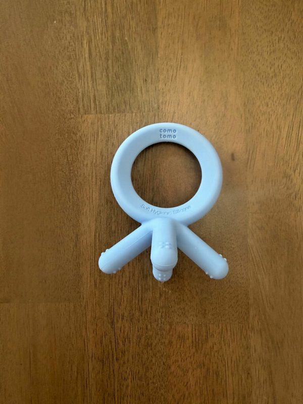 A light blue silicone teether with a ring handle and short stick arms