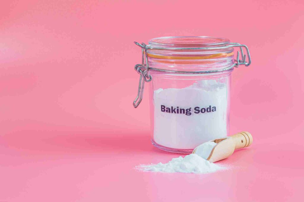 Jar and spoonful of baking soda on pink background