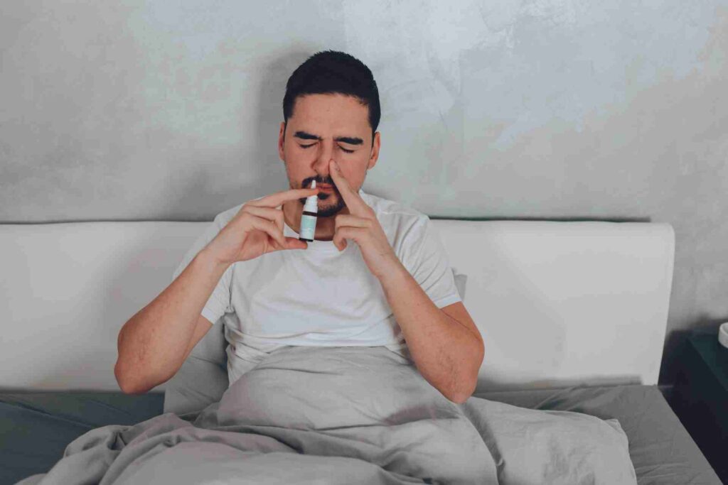 Man is sitting in his bed using a nasal spray.