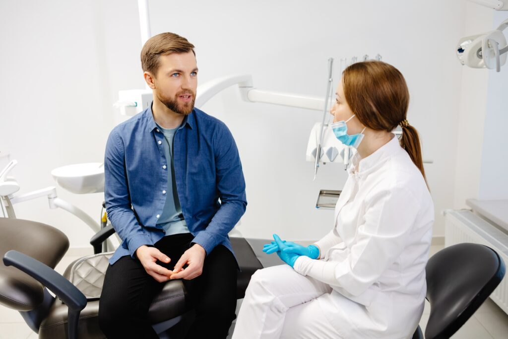 Blonde female dentist in dental office talking with male patient and preparing for treatment.