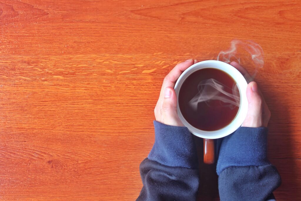 Top view of hands holding cup of coffee on wooden table.