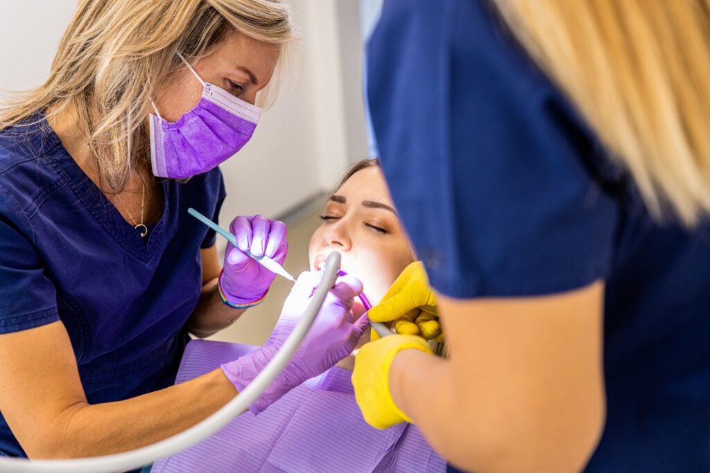Female dentist with assistant working in dental clinic examining patient teeth.