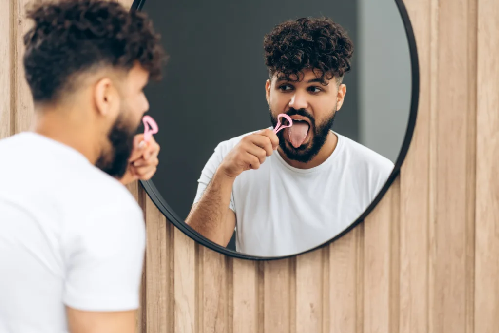 Man Cleans Tongue with Scraper in the Bathroom